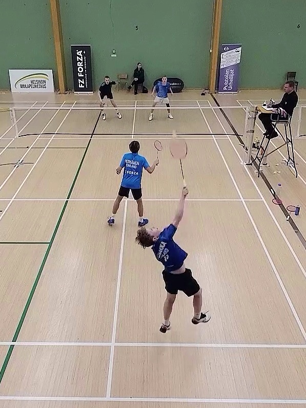 Sulkapallokilpailun nelinpeli, jossa yksi pelaaja lyö hyppysmashiä ja hänen parinsa vahtii etukenttää. Toisen puolen pari puolustaa vierekkäin. Tuomari tarkkailee peliä tuomarituolista.